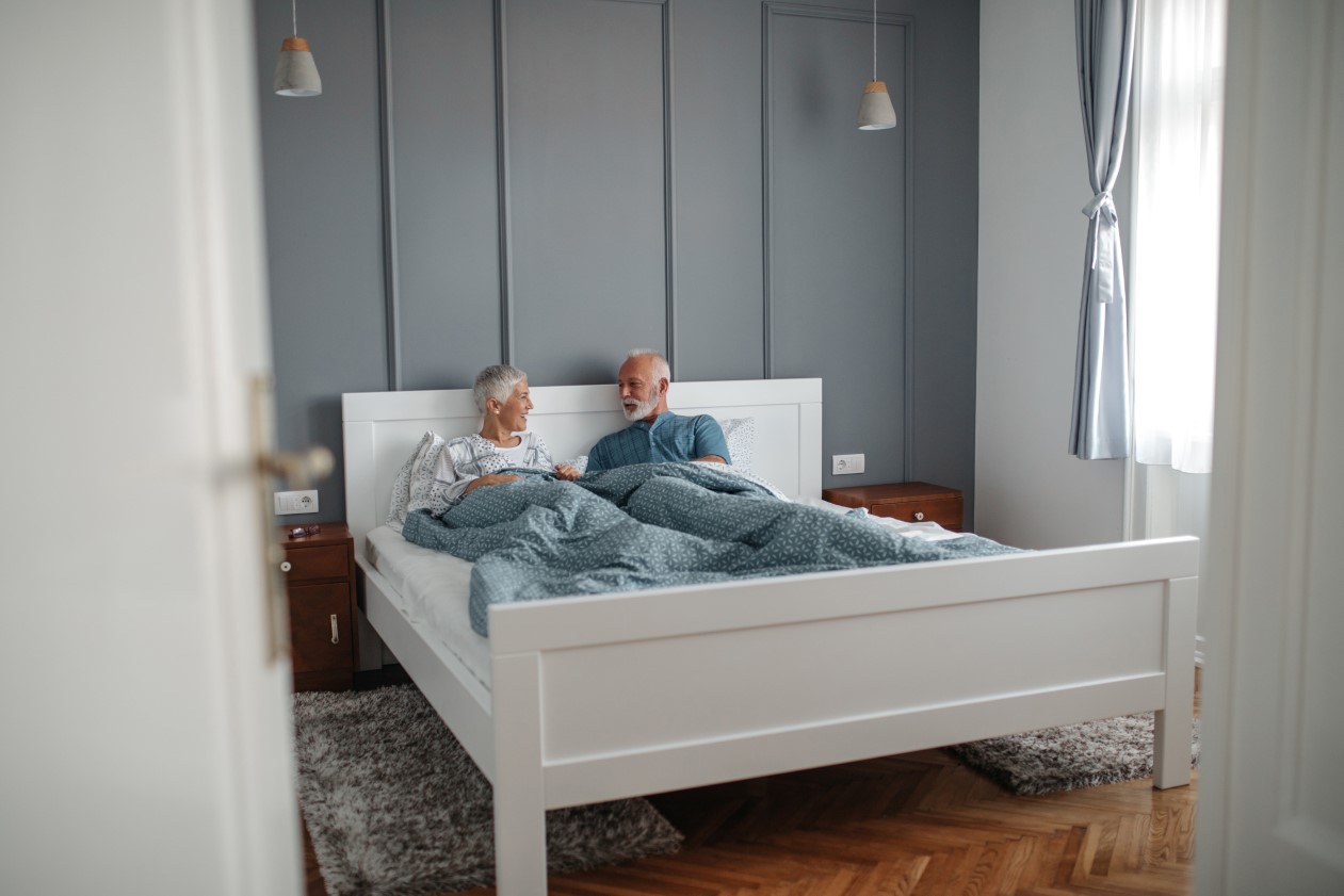 Mężczyzna leżący w łóżku z podciągniętą nogą, masujący ją, co sugeruje problem z drętwieniem lub mrowieniem nóg podczas snu.